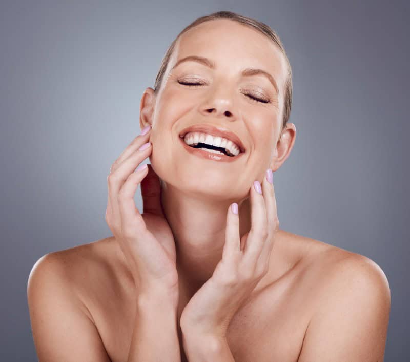 happy beautiful woman smiling with her eyes closed and hands touching her silky face, advertising profhilo treatment at Rathfarnham Medical